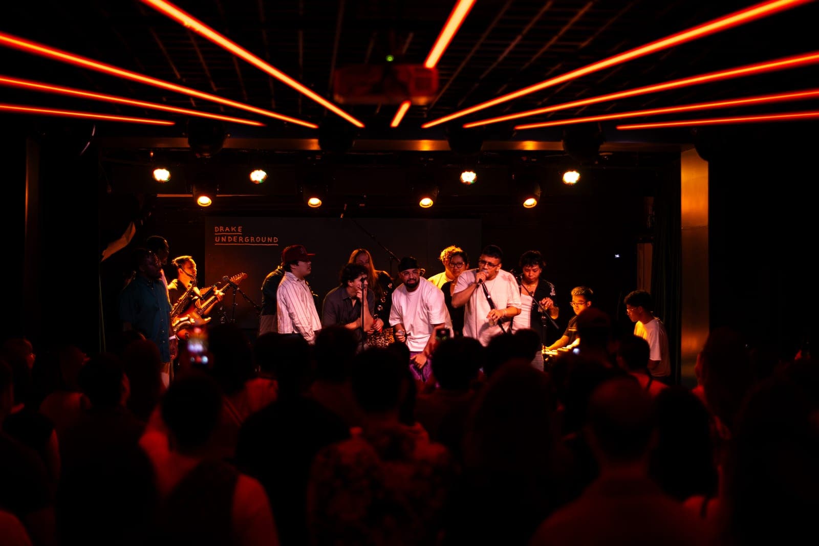The Takes a Village collective fill the stage under orange lights at The Drake Underground in Toronto