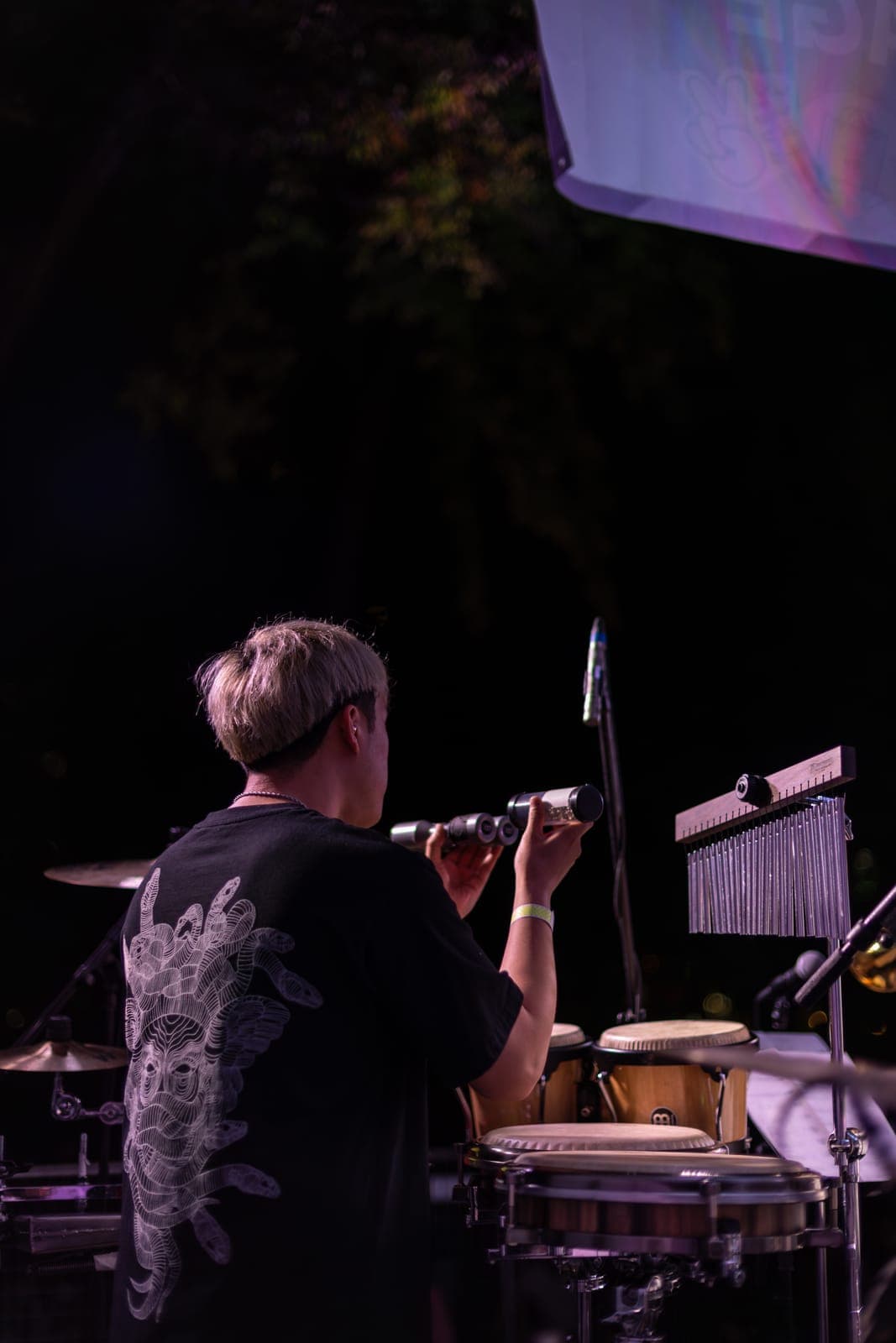 A percussionist plays wind chimes at the congas, back to the camera, during Duck Society's night set