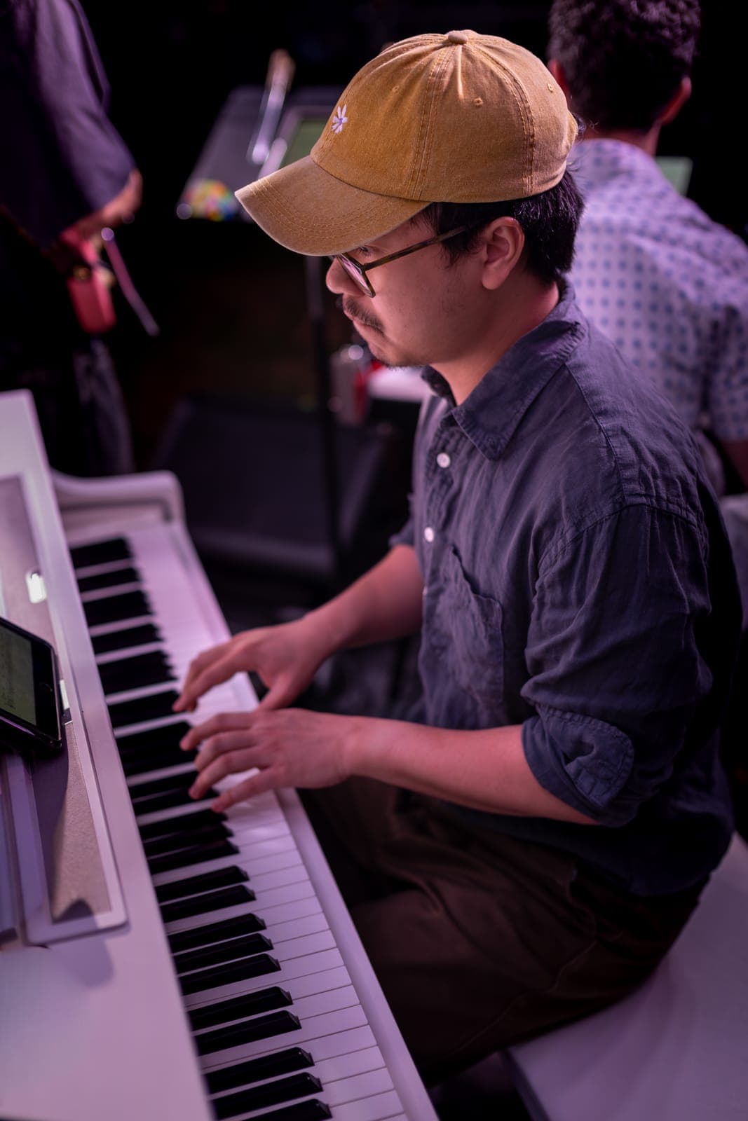 Duck Society's keyboardist, in a mustard cap and glasses, leans into the keys during the set