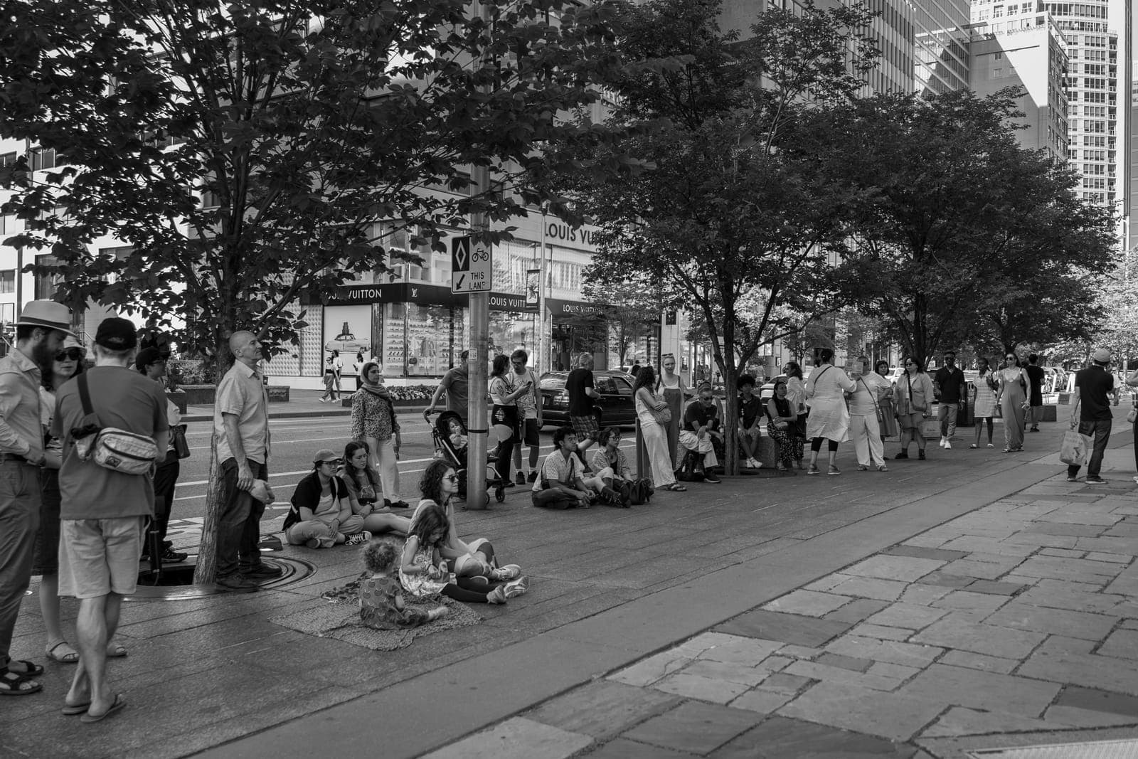 Passersby gather under the trees along Yorkville's Avenue Road to catch the sidewalk set, a Louis Vuitton storefront across the street