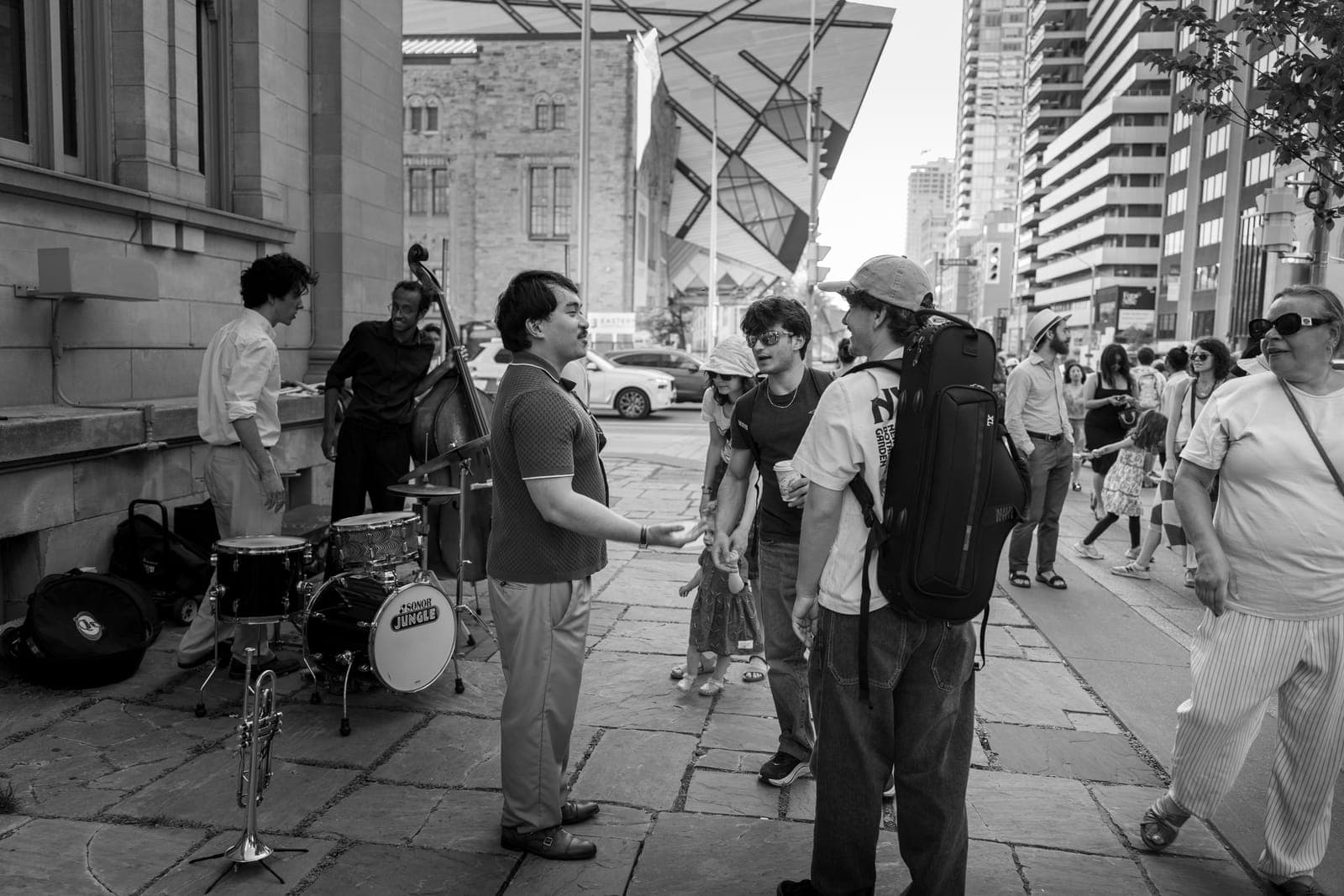 After the set the trumpeter chats with two young passersby while the rest of the trio packs up, the Royal Ontario Museum's crystal rising behind them
