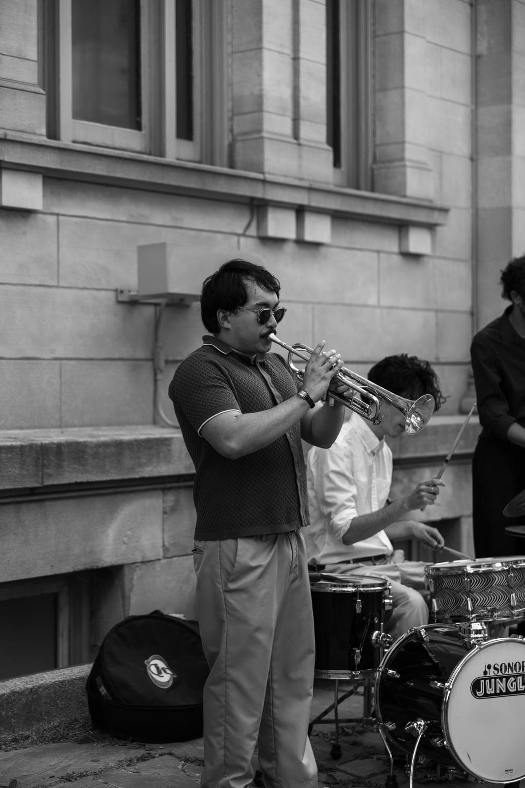 The trumpeter, in round sunglasses, digs into a solo as the drummer plays behind him