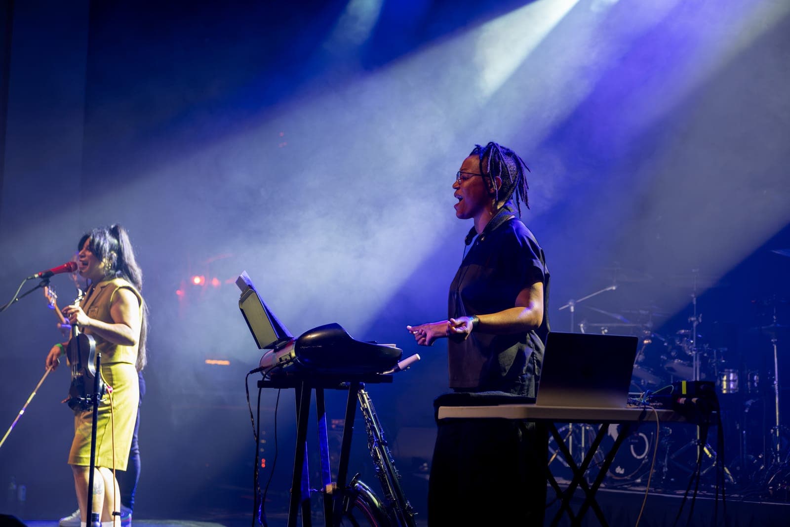 Maya Killtron plays electric violin at left while a bandmate sings over a keyboard rig in a wash of blue light