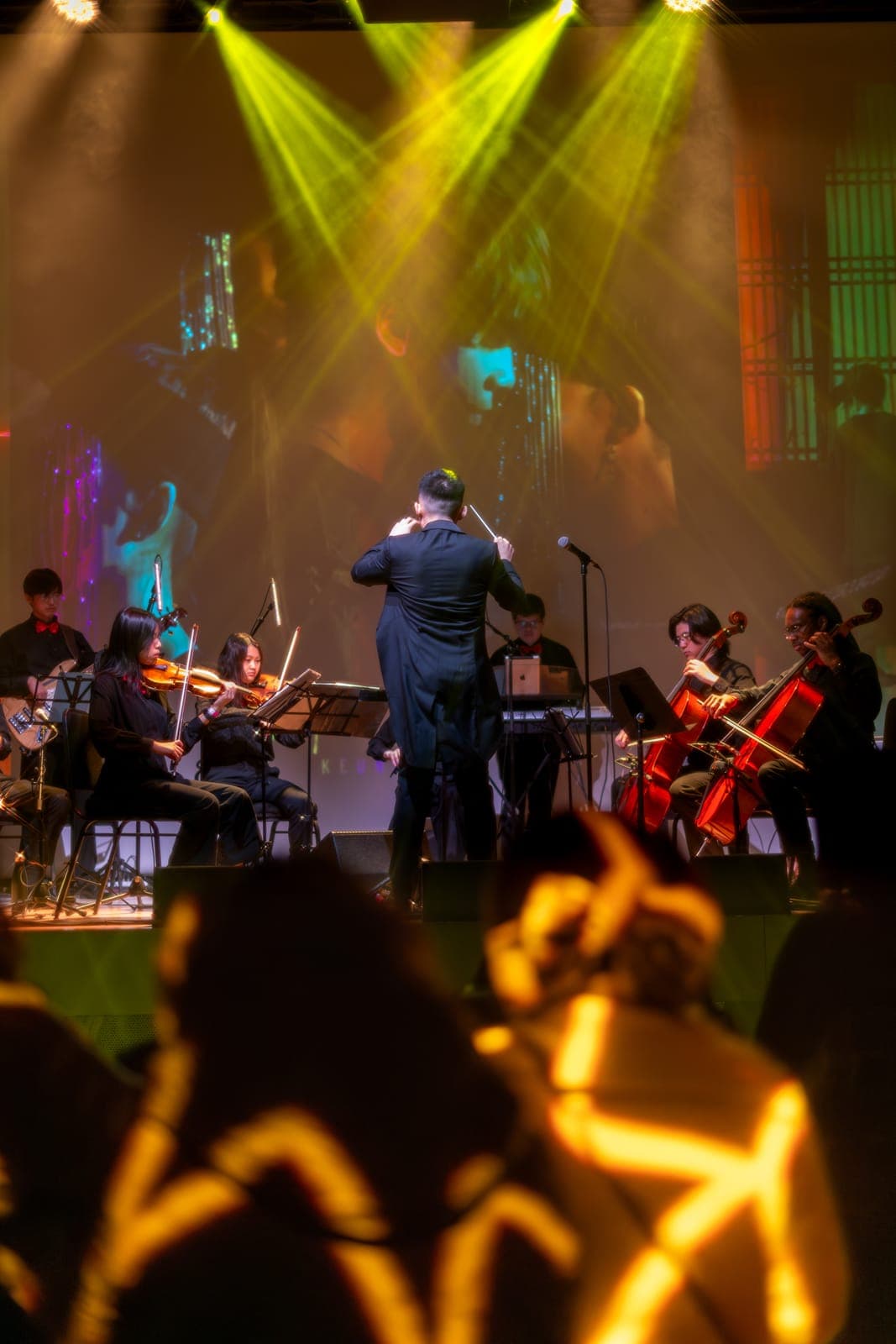 The conductor leads the Toronto Pops Orchestra under green and amber beams at the Keung To fan event at TD Music Hall, Toronto