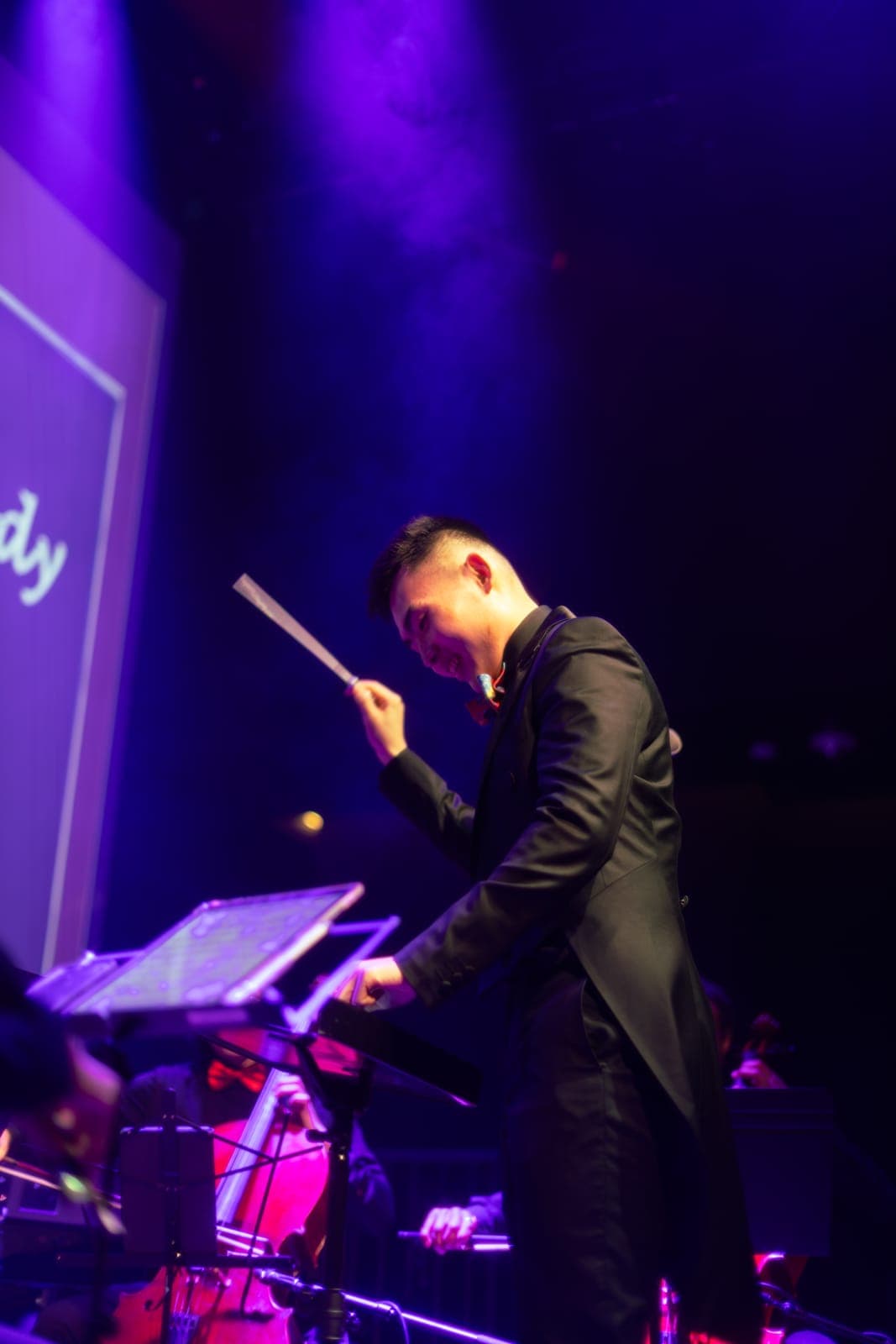 The conductor raises his baton over the score in a black tailcoat under purple light at TD Music Hall in Toronto