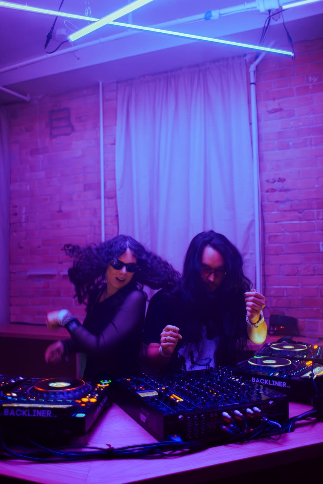 Two DJs dance behind the decks during the Indie Sleaze set under purple light at Rhythm in Toronto