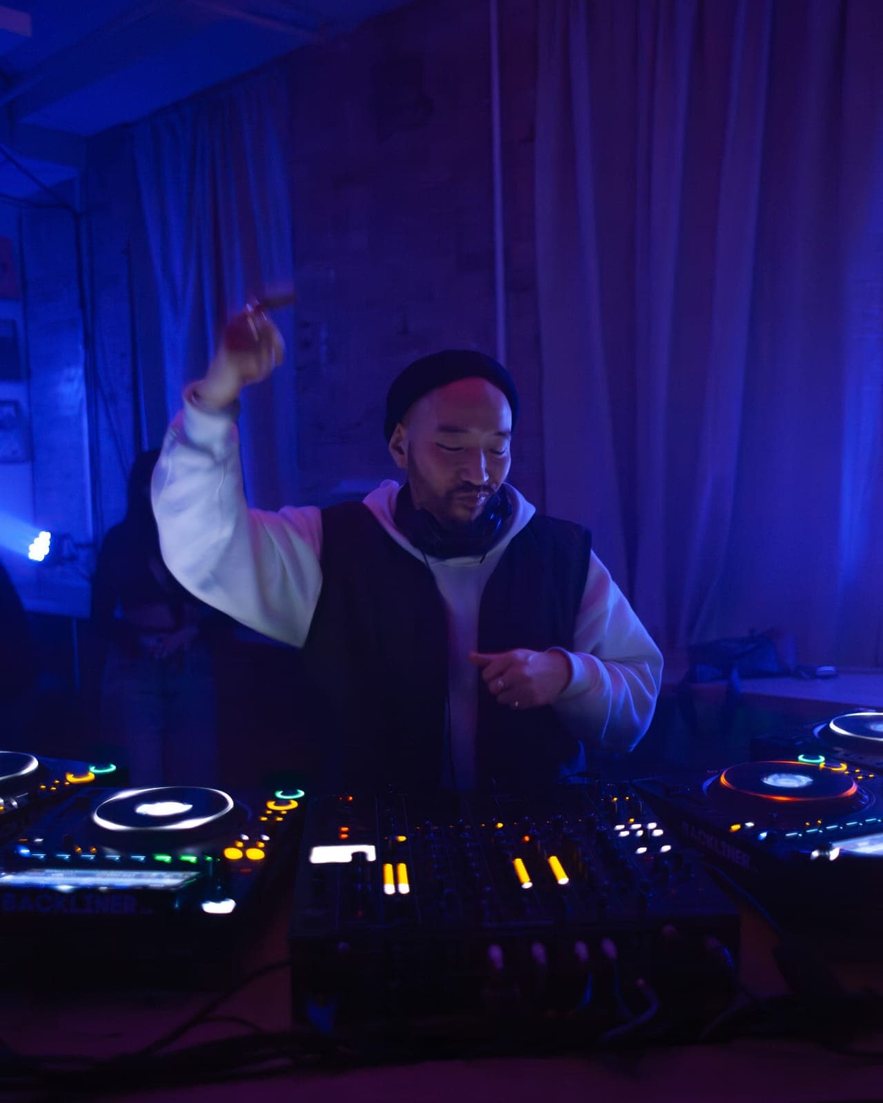 Pat Lok points upward while mixing in a beanie under blue light at Rhythm in Toronto