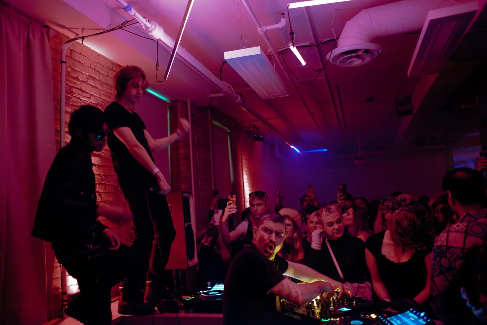 Al-P and iHeartLUSTER hype the crowd from the DJ booth, two dancers up on a ledge, at Rhythm in Toronto