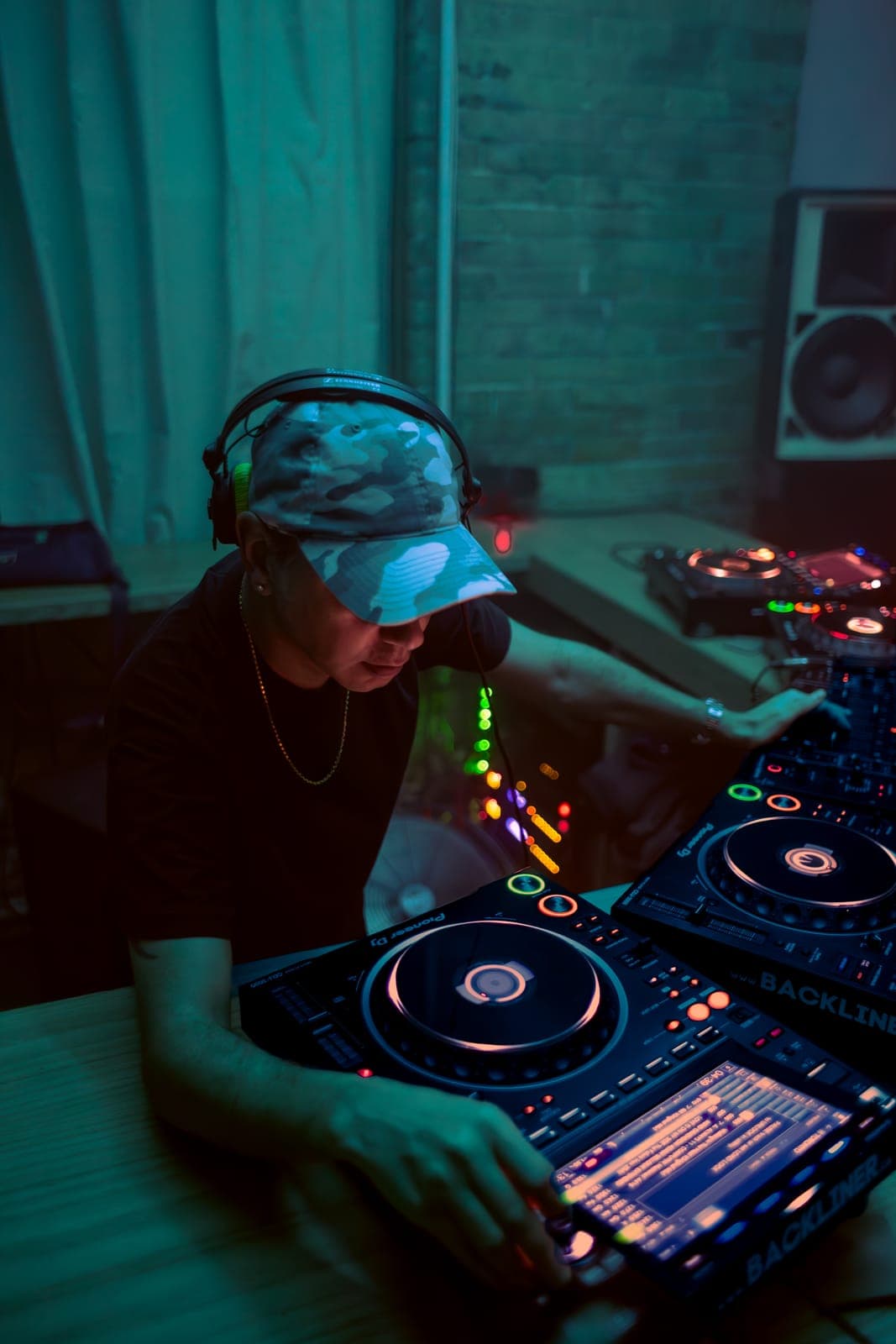 Tiga leans over the Backliner CDJs in a camo cap under teal light at Rhythm in Toronto